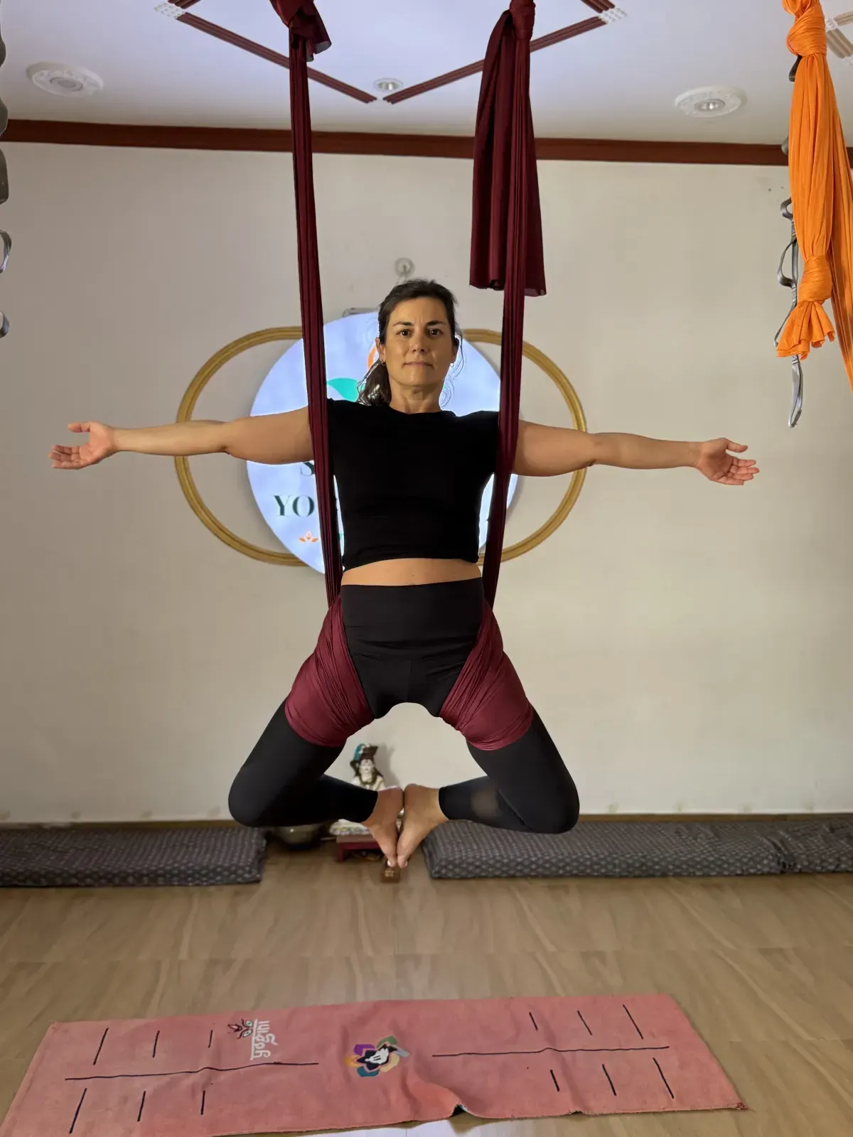 Student seated in the aerial hammock sling in butterfly pose, soles of the feet together and arms spread wide