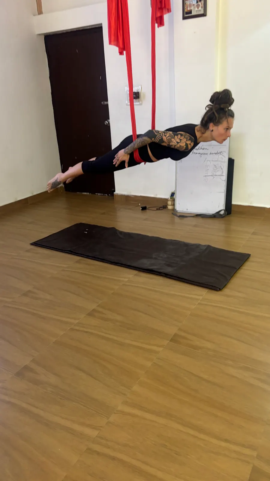 Student flying horizontally in superman pose, hips supported by a red aerial hammock, arms reaching forward