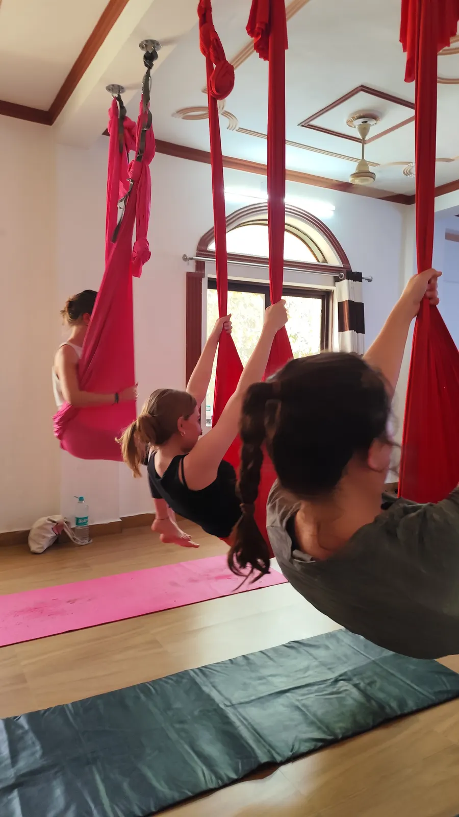 Group of students leaning into their red aerial hammocks together during an aerial yoga teacher training class