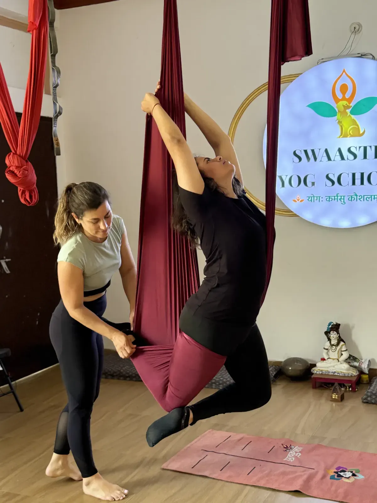 Aerial yoga teacher spotting a student as she leans back into a supported hammock backbend during teacher training in Rishikesh