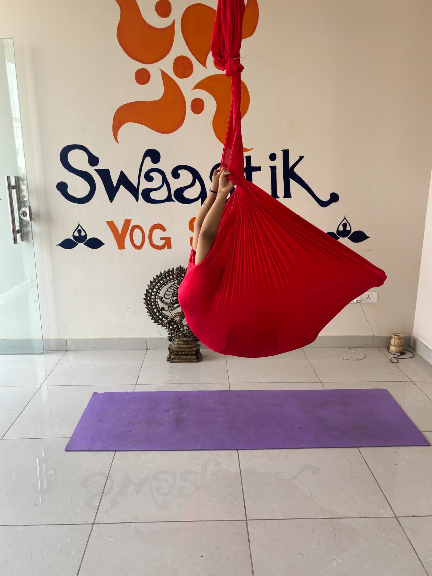 A student lying back in an aerial hammock, fully supported and relaxed — aerial yoga suits every body